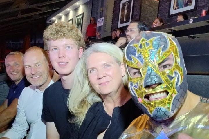 다채로운 색상의 복장을 한 마스크 착용자를 포함한 일행이 활기찬 실내 환경에 앉아 미소를 짓고 있습니다.