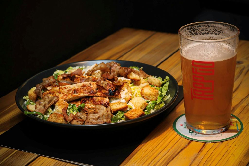 맥주 한 잔 옆 나무 테이블에 구운 치킨과 크루통을 곁들인 샐러드 한 그릇.