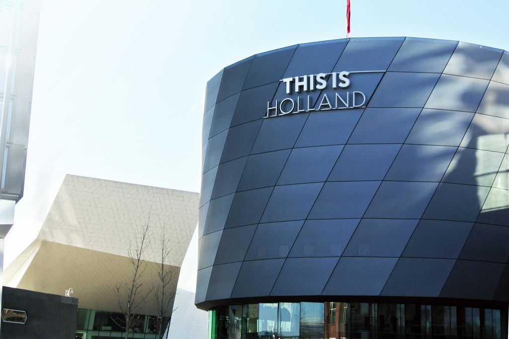 "THIS IS HOLLAND" 라는 텍스트가 표시된 어둡고 기하학적인 패턴의 외관이 있는 현대적인 건물입니다.
