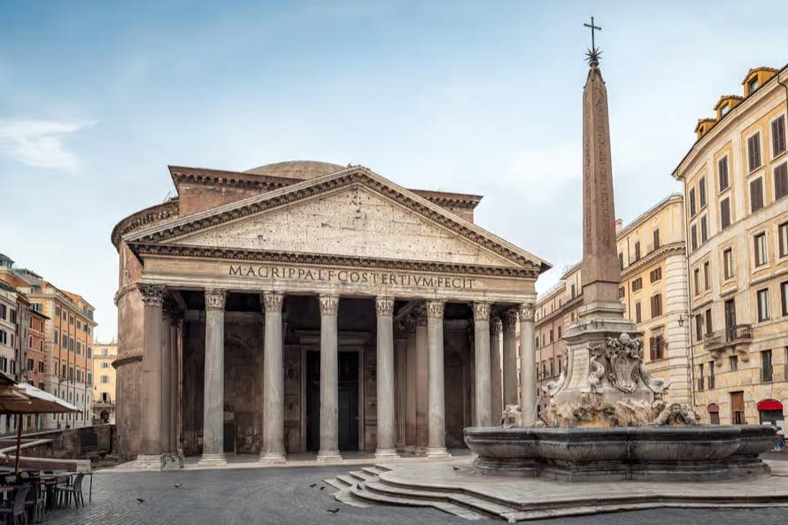 도심 광장의 오벨리스크와 분수 옆 외관에 높은 기둥과 비문이 있는 고대 건물.