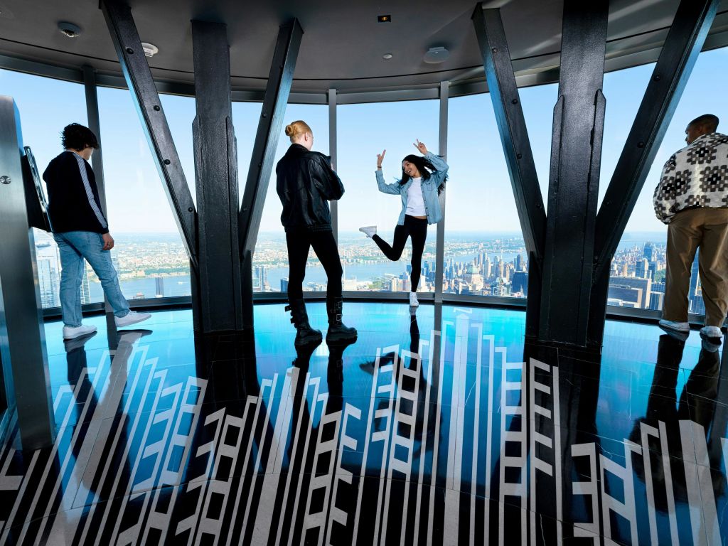 도시 전망을 감상할 수 있는 유리 전망대에서 두 사람이 검은 대들보와 무늬가 있는 바닥을 받치고 있습니다.