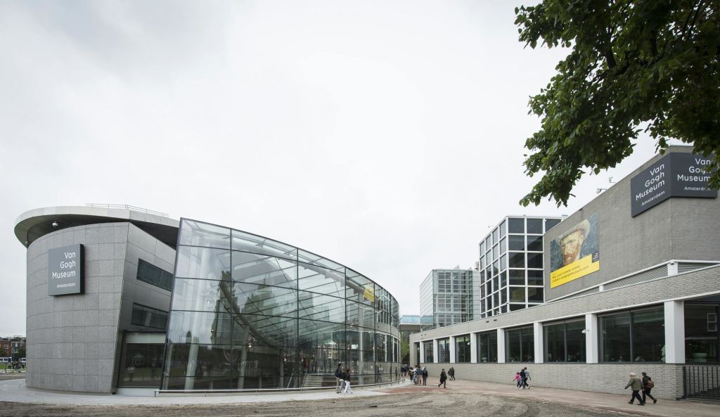 그리드 창문이 있는 정사각형 건물에 인접한 곡선형 외관이 있는 현대적인 유리 건물. 근처를 걷는 사람이 거의 없습니다.