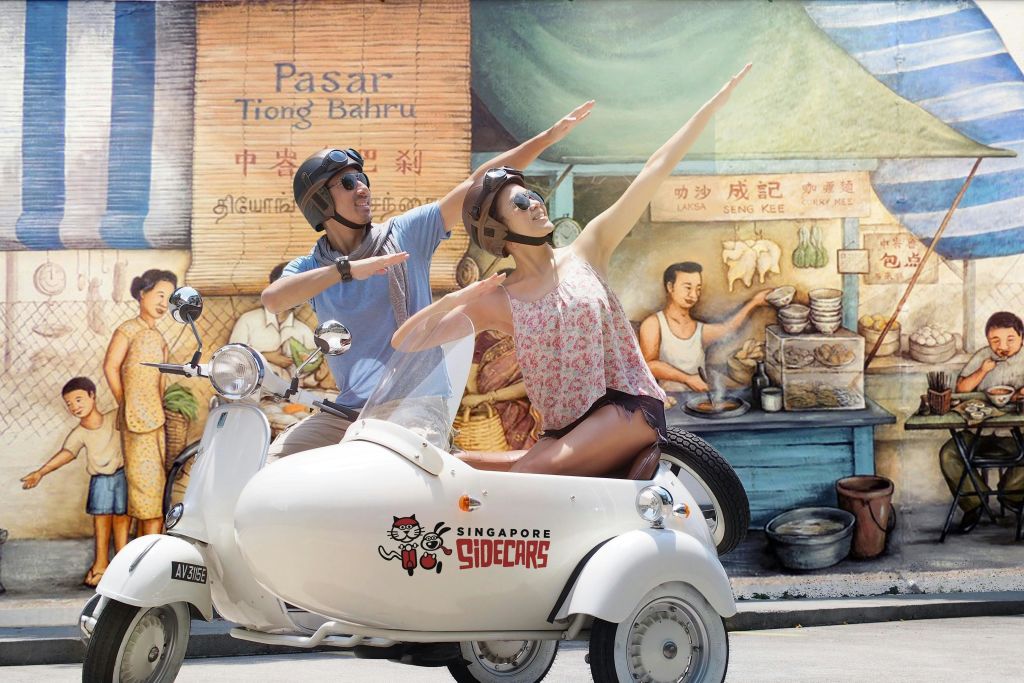 시끌벅적한 길거리 음식 가판대 뒤편의 벽화를 모방한 두 사람이 하얀 사이드카에서 포즈를 취하고 있습니다.