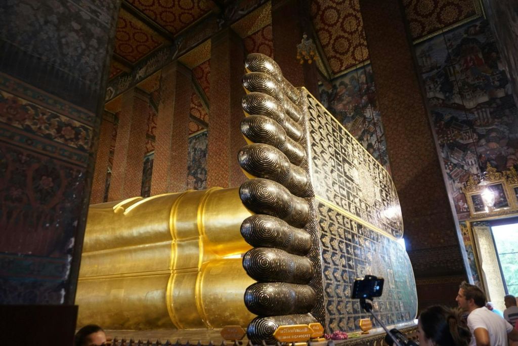 화려한 사원 내부에서 정교한 문양으로 장식된 커다란 황금 불상의 발을 클로즈업했습니다.
