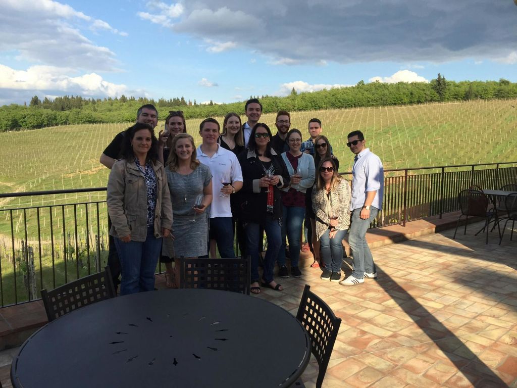 탁한 하늘을 배경으로 포도밭이 내려다보이는 파티오에 서 있는 한 무리의 사람들.