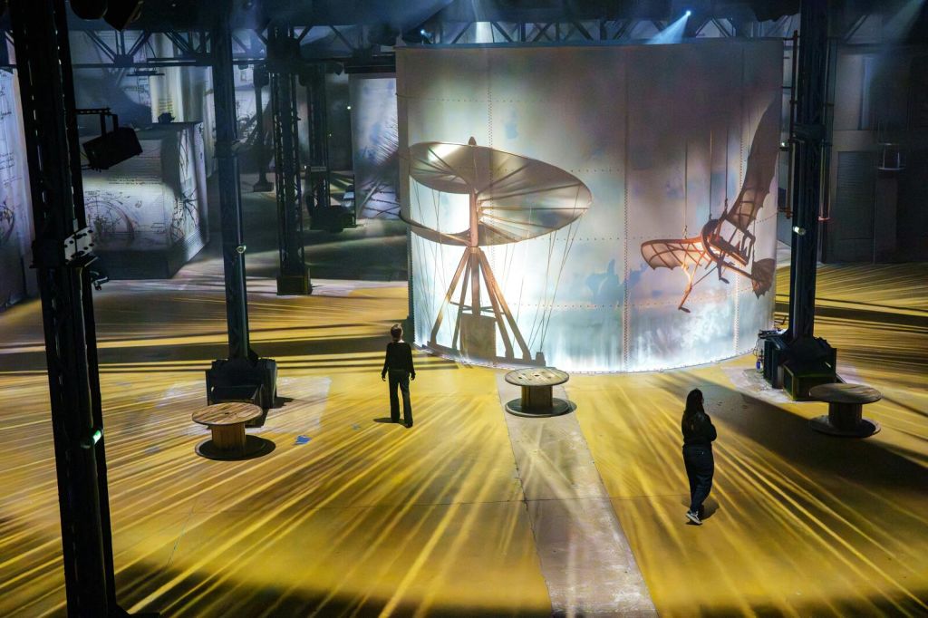 항공을 주제로 한 이미지를 묘사한 대형 조명 스크린이 있는 갤러리 공간으로, 개인이 전시관을 돌아다니고 있습니다.