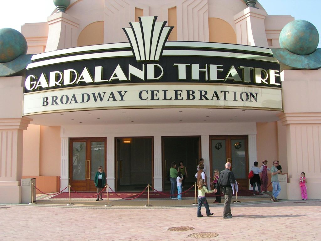 "ARDALAND THEATRE - BROADWAY CELEBRATION" 이라고 적힌 마키가 있는 극장 입구 앞을 걷는 사람들.