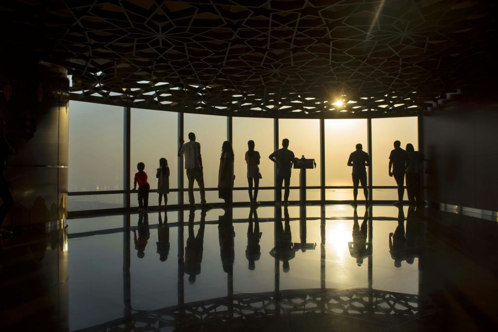 실루엣의 사람들이 해가 질 무렵 커다란 창문 옆에 서 있습니다. 무늬가 있는 천장과 반사 바닥이 있는 방에서 말이죠.