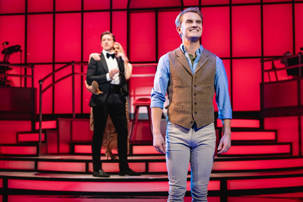 정장 차림의 두 사람이 불이 켜진 무대 뒤에서 가까이 서서 웃고 있습니다.