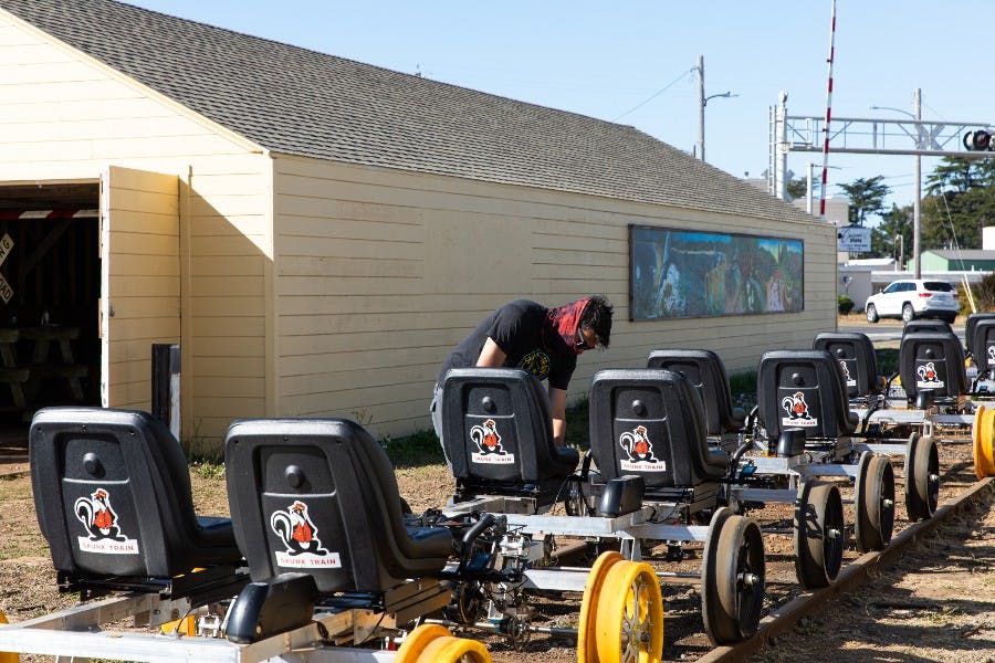 사람은 화창한 날 벽화가 그려진 건물 옆에서 스컹크 로고가 있는 놀이공원 승차 좌석을 일렬로 점검합니다.