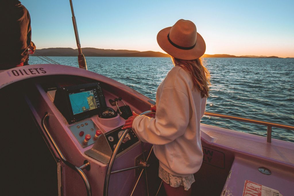 해 질 녘, 물과 먼 산의 전망을 감상하며 보트를 조종하는 모자를 쓴 사람.
