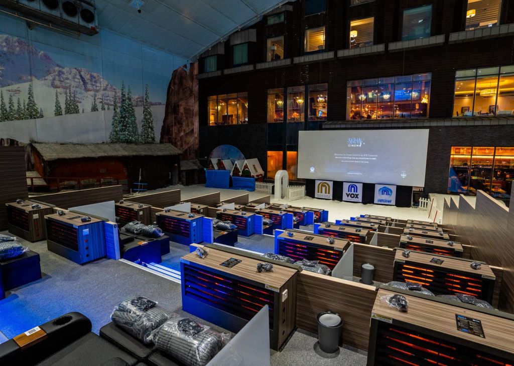 아늑한 좌석과 담요를 갖춘 실내 극장은 투사 스크린을 향하고 있습니다. 산을 테마로 한 인테리어와 커다란 창문을 배경으로 합니다.