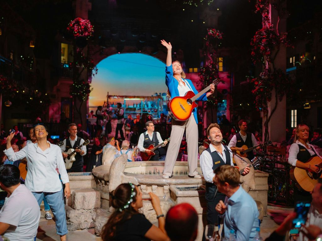 조명이 켜진 공연장에서 뮤지션과 청중으로 둘러싸인 분수대에 서 있는 기타리스트와 함께 생동감 넘치는 공연을 즐겨보세요.