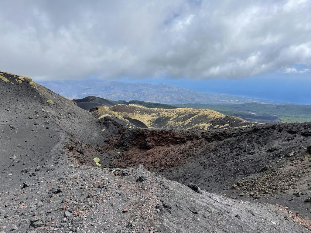 부분적으로 흐린 하늘 아래 암석 지형과 분화구가 있는 화산 지형. 멀리 산과 계곡이 보입니다.