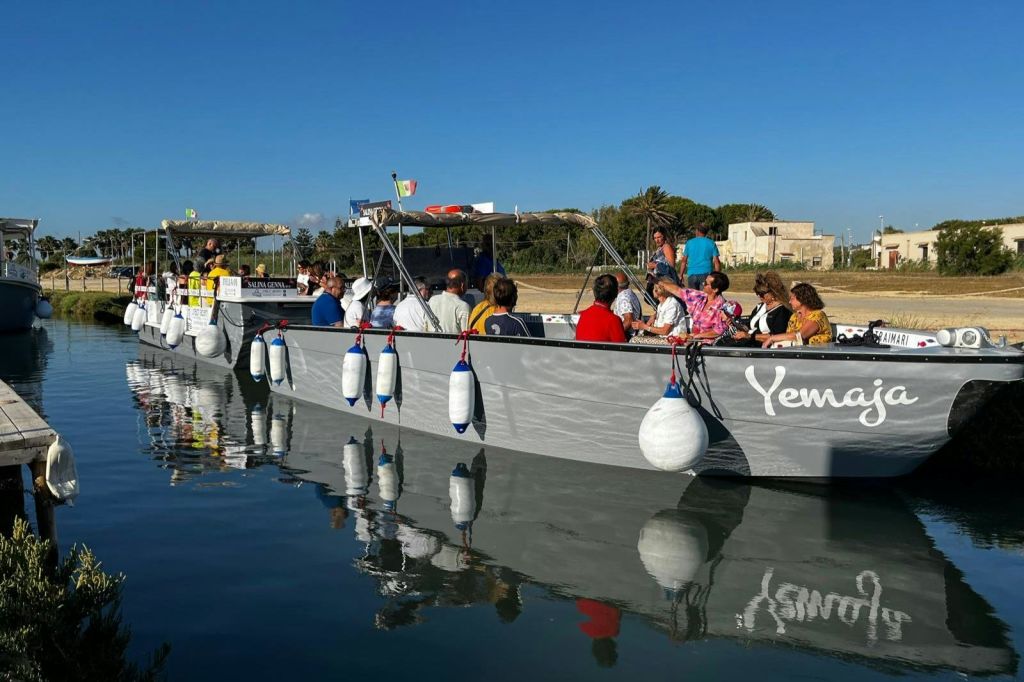 맑고 푸른 하늘 아래 잔잔한 물 위에 떠 있는 '예마' 라는 이름의 회색 보트에 앉은 한 무리의 사람들.