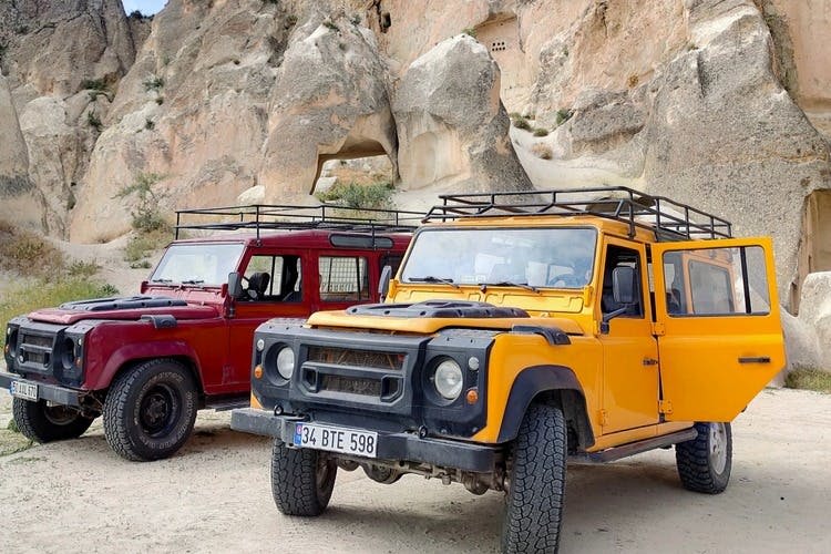 빨간색과 노란색 두 대의 오프로드 차량이 동굴과 같은 지층이 있는 바위 절벽 앞에 주차되어 있습니다.