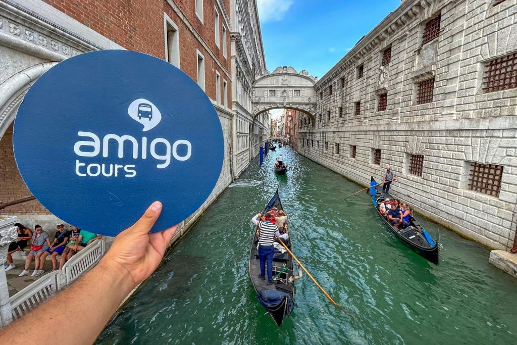 곤돌라와 탄식의 다리를 배경으로 한 베네치아의 운하. '아미고 투어 (amigo tours)' 라고 적힌 표지판을 들고 있는 손.