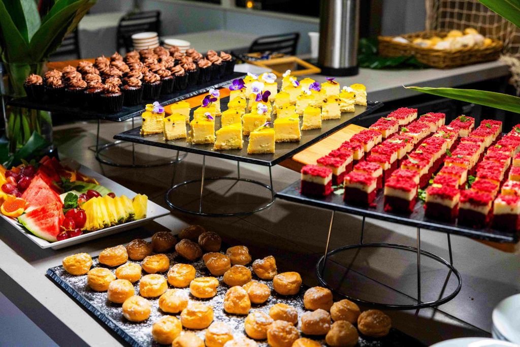 초콜릿 컵케이크, 꽃이 달린 노란 케이크, 빨간 상판 바, 가루로 만든 도넛 구멍 등 트레이에 담긴 다양한 디저트.