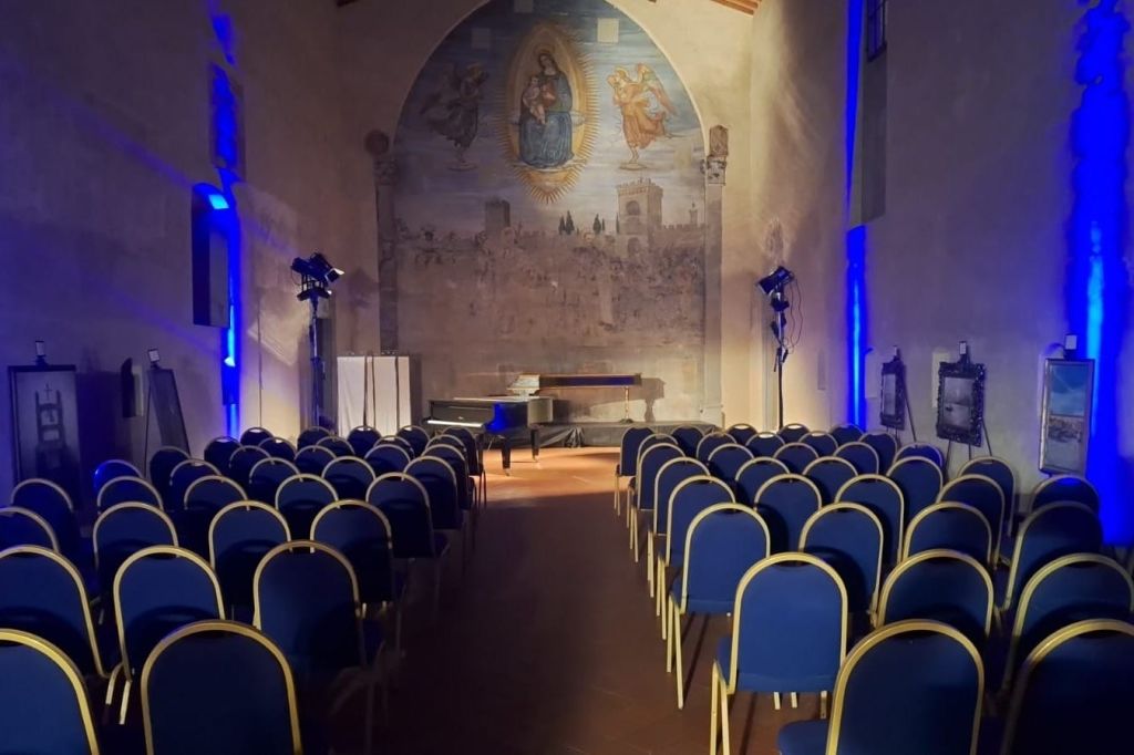 푸른색 의자가 줄지어 있는 빈 강당으로, 무대에는 그랜드 피아노와 벽화를 배경으로 한 벽이 있습니다.