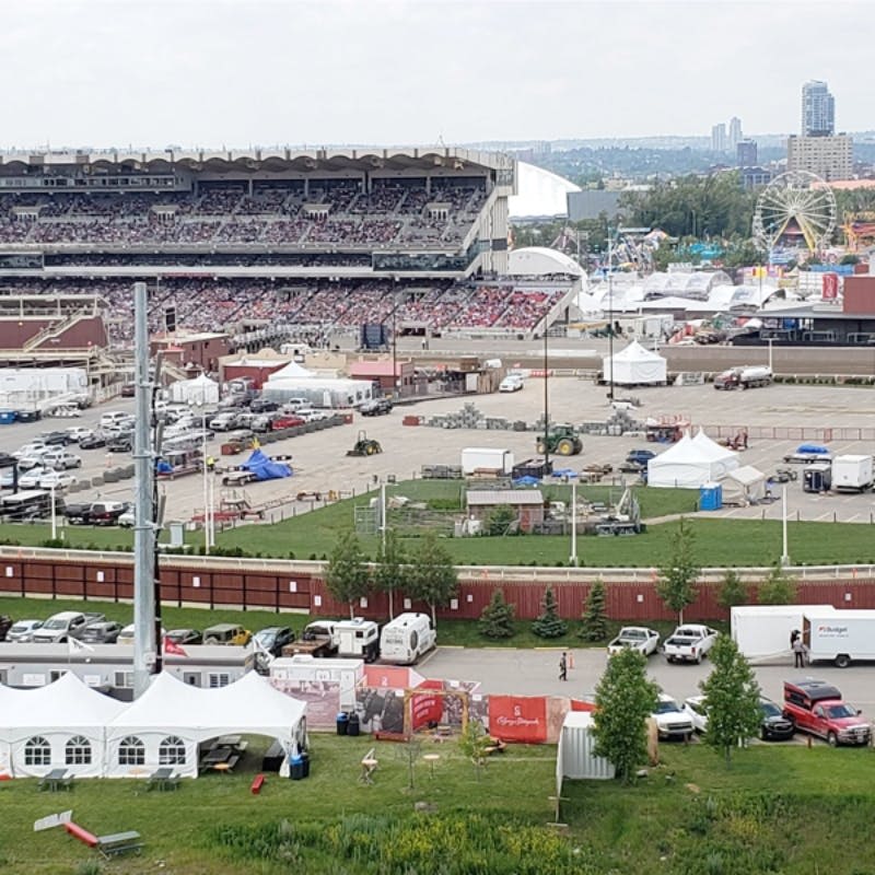 놀이기구와 텐트를 갖춘 인접한 박람회가 있는 붐비는 경기장. 전경에 보이는 주차장 및 여러 건물.