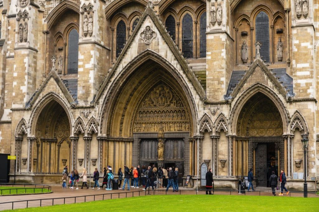 입구 위로 아치형 출입구와 정교한 조각이 있는 유서 깊은 석조 성당으로 걸어 들어가는 사람들.
