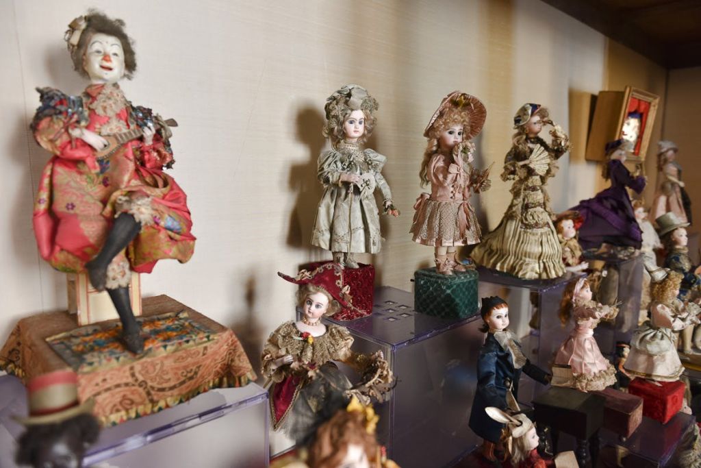 투명 스탠드와 천으로 덮인 표면에 정교한 옷을 입은 빈티지 인형이 전시되어 있습니다.