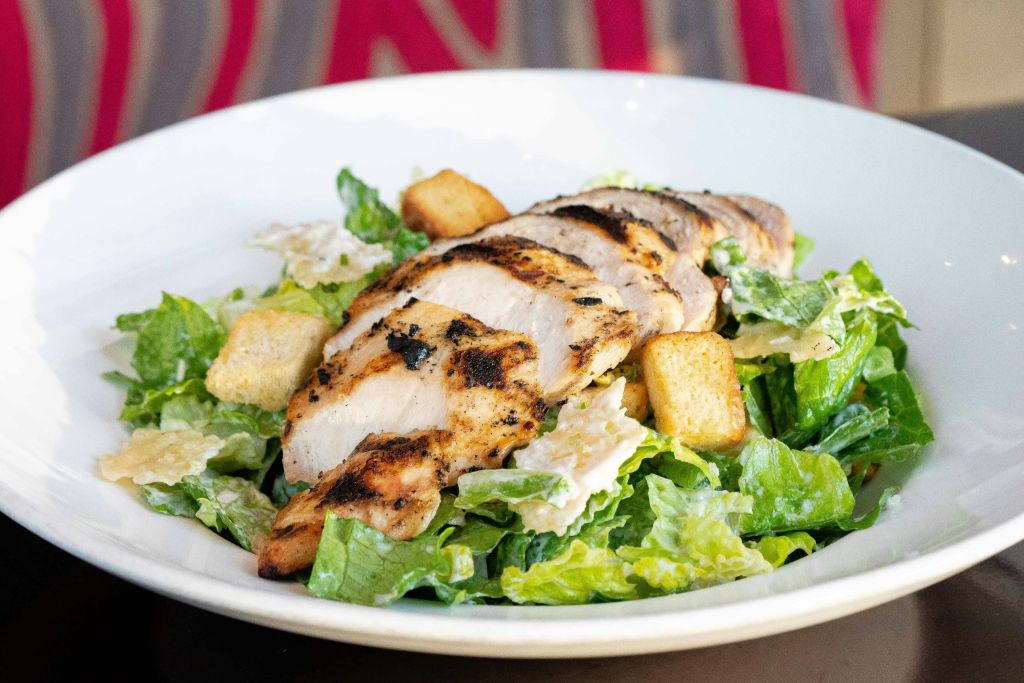 흰 접시에 구운 치킨 슬라이스, 크루통, 로메인 양상추를 곁들인 시저 샐러드.