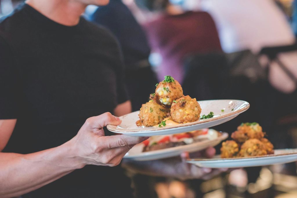 레스토랑에서 약초로 장식된 튀긴 공을 포함한 음식 접시를 들고 있는 사람.