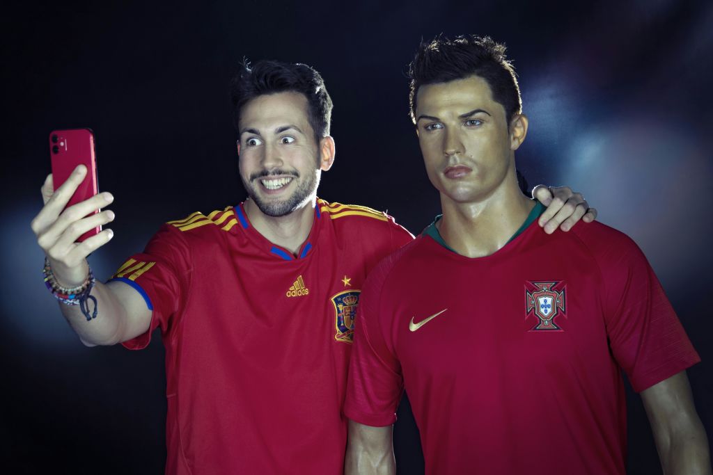 빨간색 스페인 축구 유니폼을 입은 남성이 빨간색 포르투갈 축구 유니폼을 입은 왁스 피규어와 함께 셀카를 찍고 있습니다.