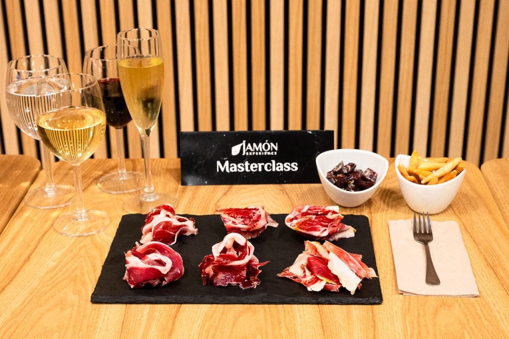 햄 테이스팅 마스터클래스를 위한 테이블 세트로, 슬레이트에 햄 슬라이스, 와인잔, 작은 측면 그릇이 있습니다.