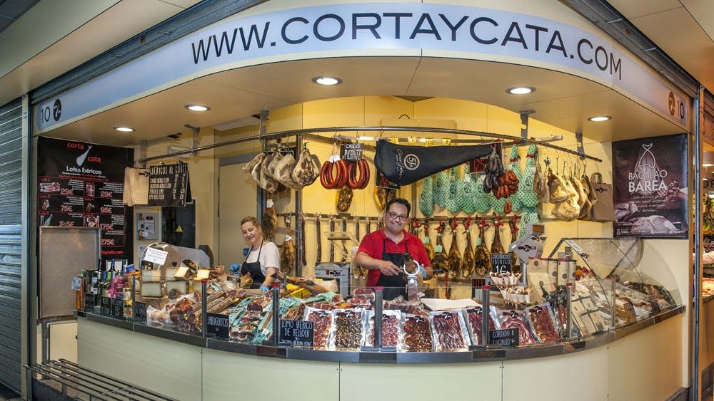 고기와 소시지가 진열된 델리 카운터에는 미소 짓는 직원 2명과 얇게 썬 고기가 한 명씩 있습니다.