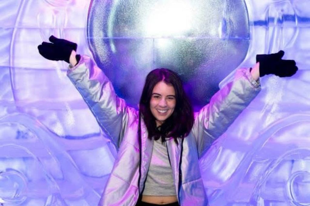 활기찬 보라색과 파란색 불빛을 배경으로 반사 재킷을 입고 팔을 들어 올린 채 미소를 짓고 포즈를 취하는 사람.