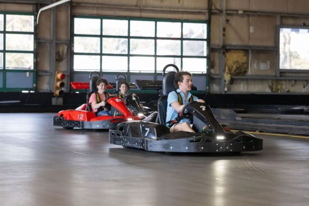 콘크리트 바닥과 커다란 창문을 배경으로 커다란 실내 트랙에서 고카트를 운전하는 세 사람.