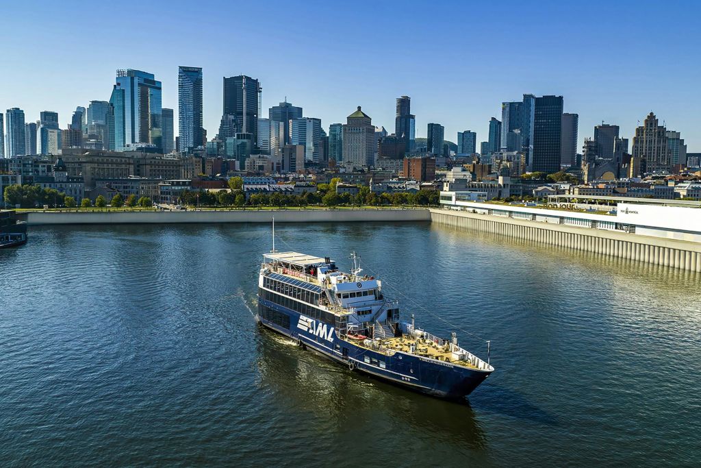 맑고 푸른 하늘 아래 도시 스카이라인을 배경으로 항구를 항해하는 "AML" 이라는 이름의 페리입니다.