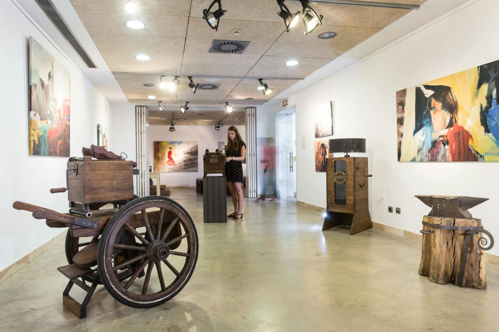 검은 드레스를 입은 여성이 트랙 조명 아래 흰색 벽에 다양한 조각과 그림이 있는 미술관을 탐험합니다.