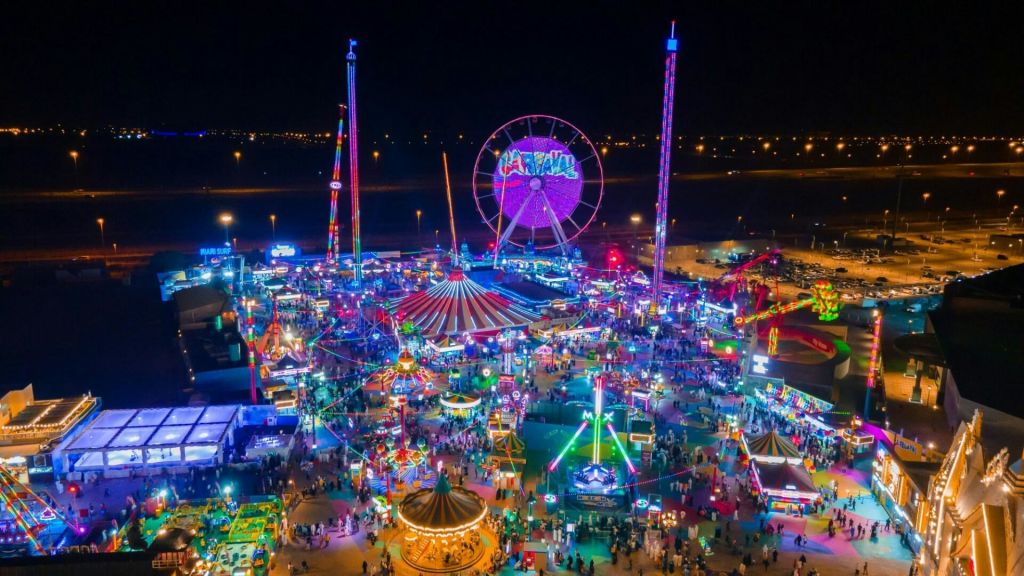화려한 조명, 대관람차, 회전목마를 포함한 놀이기구, 수많은 사람들이 어우러진 활기찬 야간 카니발입니다.
