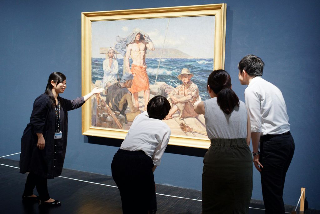 세 사람은 보트에서 선원의 대형 액자 그림을 보며 가이드가 세부 사항을 지적합니다.