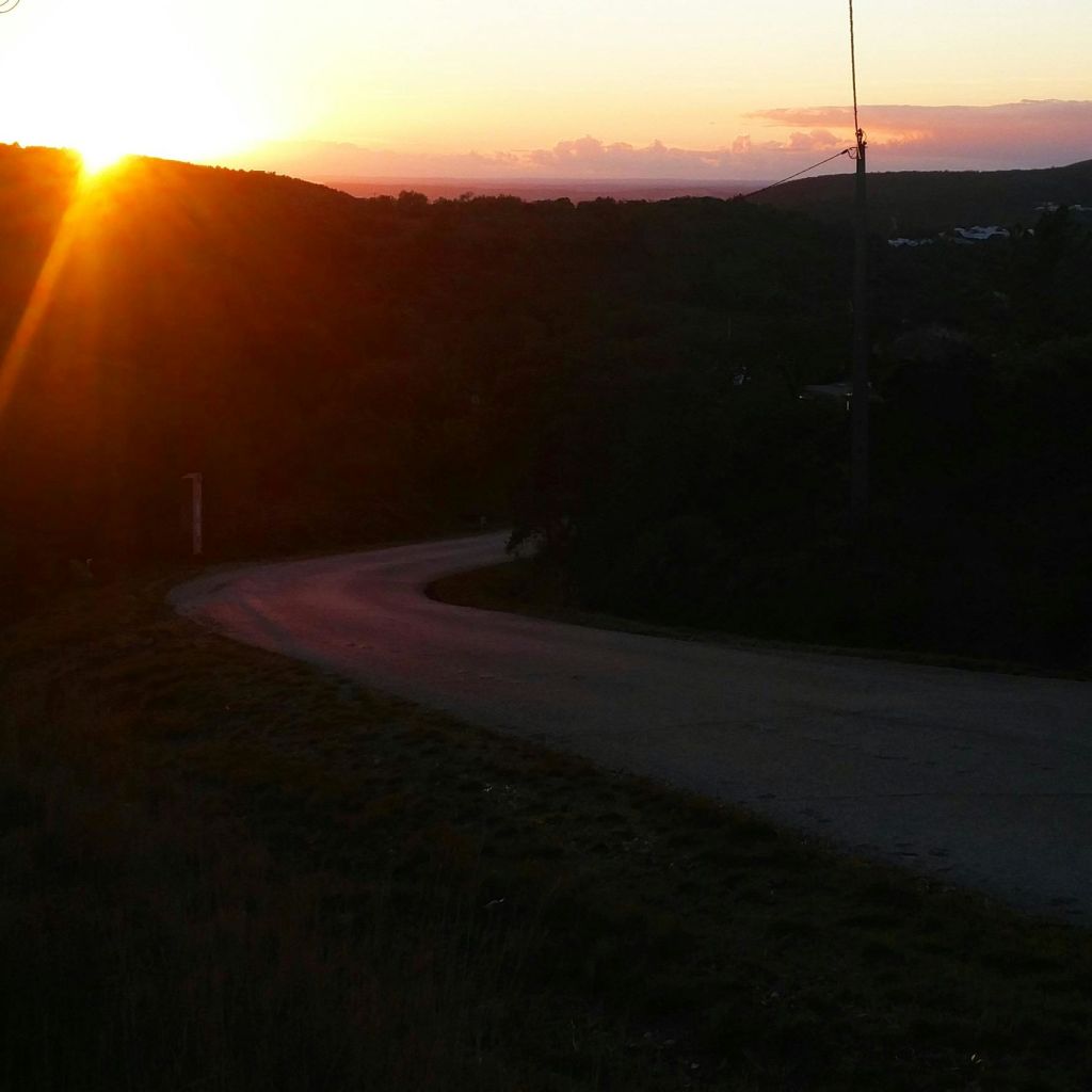 구불구불한 도로가 저 멀리 언덕을 내려다보는 석양을 비추며 어두운 조명을 뚫고 지나갑니다.