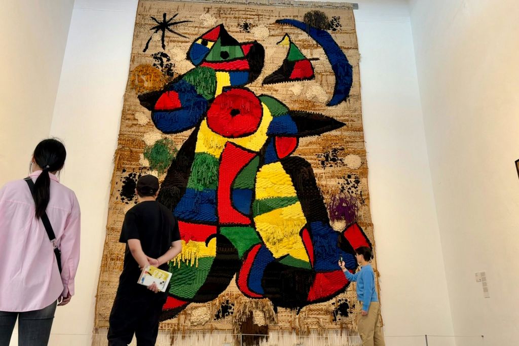 두 사람은 대담한 모양과 질감이 특징인 갤러리 벽에 설치된 크고 다채로운 추상적인 태피스트리를 관찰합니다.