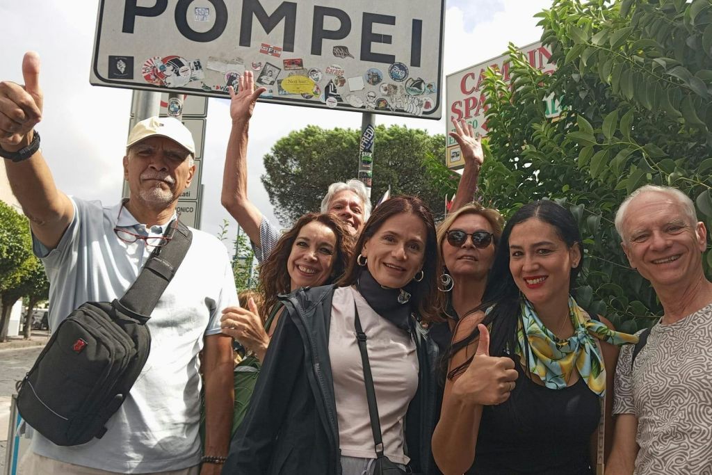 나무와 푸르름을 배경으로 '폼페이' 라고 적힌 표지판 앞에서 웃으며 포즈를 취하고 있는 여섯 명.