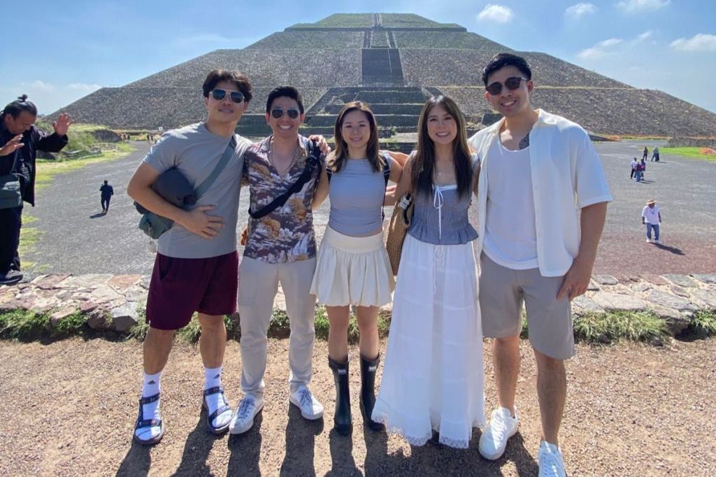 화창한 날 커다란 피라미드 앞에서 포즈를 취하는 다섯 사람. 모두가 웃으며 캐주얼한 여름 옷을 입고 있습니다.