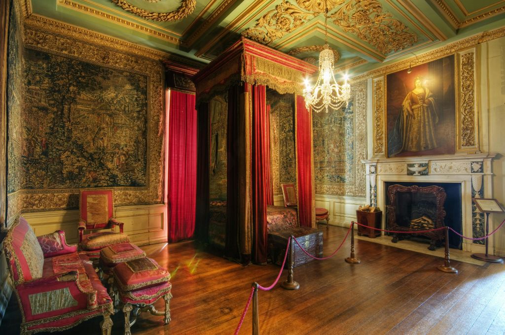 샹들리에, 빨간색 커튼이 있는 4주식 침대, 앤티크 가구, 무늬가 있는 태피스트리, 벽난로가 있는 화려한 객실입니다.