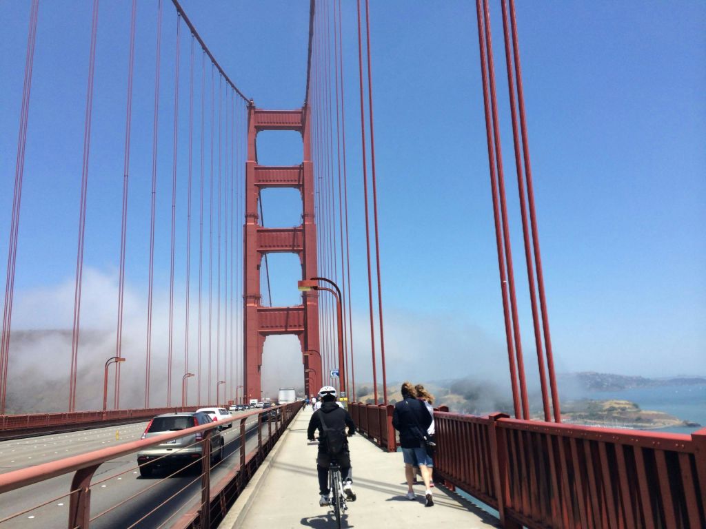 자전거를 타는 사람과 금문교를 걷는 보행자가 도로에 차를 대고 안개를 배경으로 달립니다.