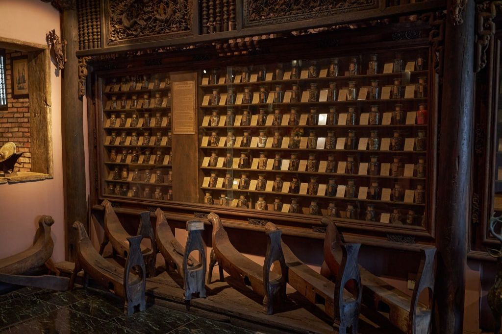 조명이 희미한 방의 화려한 벤치 뒤에 놓인 작은 병과 라벨이 줄지어 있는 나무 디스플레이 케이스.