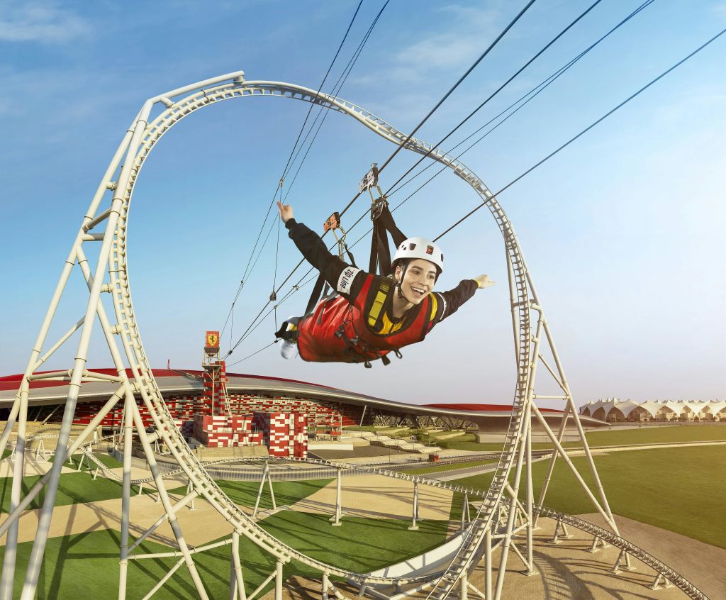 지퍼 라인 코스터에 빨간 양복과 헬멧을 쓴 사람이 화창한 날 공원의 루프를 통과하며 미소를 짓고 있습니다.