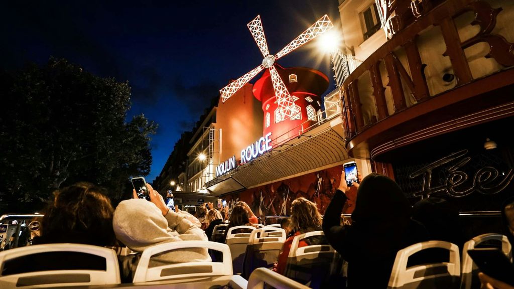 밤에 밝게 빛나는 물랑루즈 풍차를 배경으로 사진을 찍고 있는 사람들.