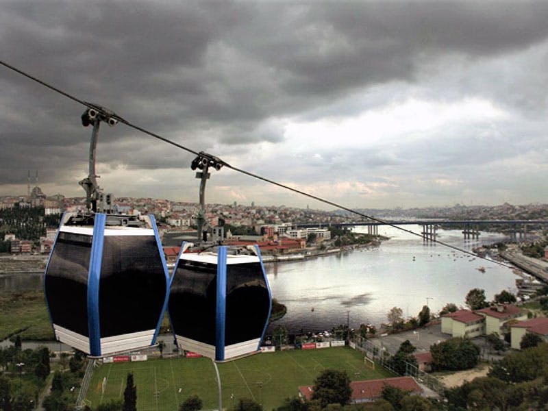 두 대의 곤돌라 리프트가 흐린 하늘 아래 도시 풍경을 배경으로 강 위에 매달려 있습니다.