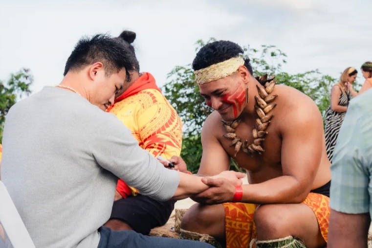 야외에서 다른 사람의 손을 잡고 의식을 치르는 전통 복장과 얼굴 페인트를 착용한 남성.