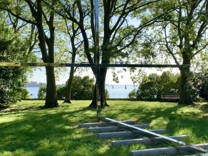 잔디가 우거진 지역의 나무 사이를 가로지르는 금속 막대가 있는 야외 장면으로, 멀리 떨어진 구조물이 있는 물줄기가 내려다보입니다.