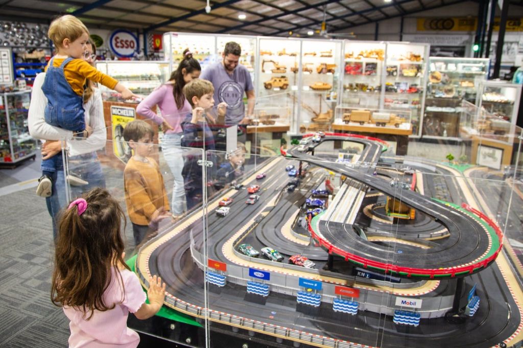 어린이와 성인은 장난감 가게에서 다양한 장난감 자동차가 전시된 모형 경주용 자동차 트랙을 구경합니다.